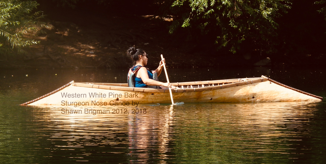 A young woman paddles a canoe through the water with lush trees in the background