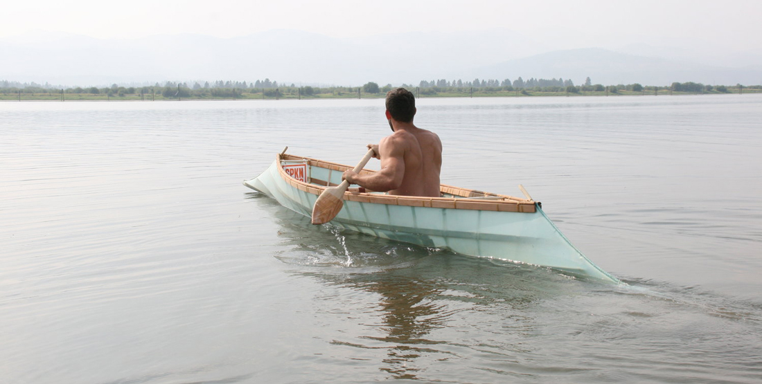 A young man paddles the canoe he built