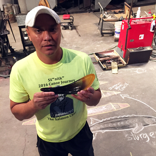 A man holds a glass buffalo horn spoon he made in the hot shop