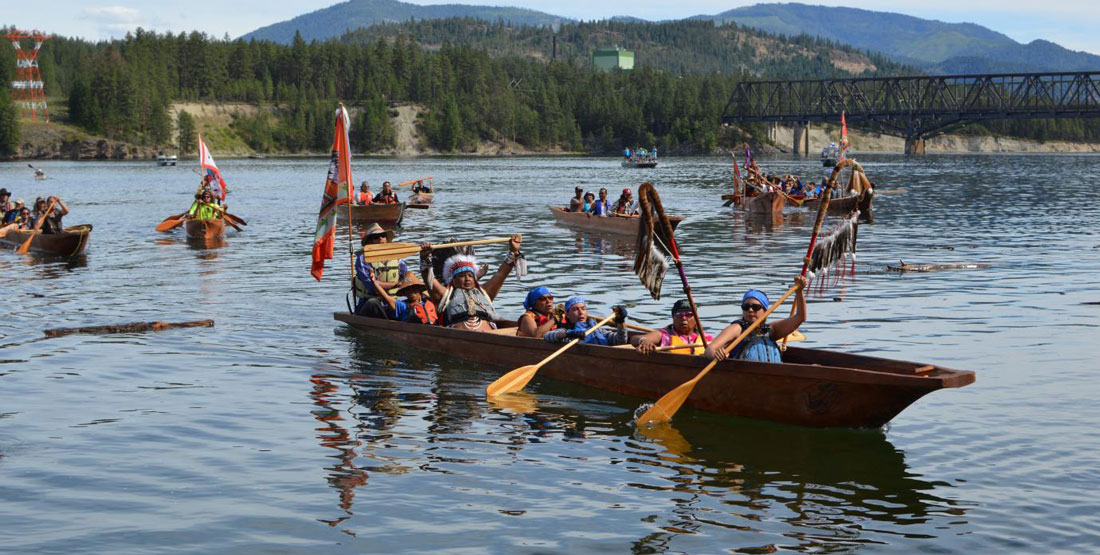 A group of people in traditional native clothes paddle a canoe