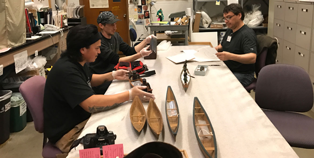 Three men sit around a table examining model boats