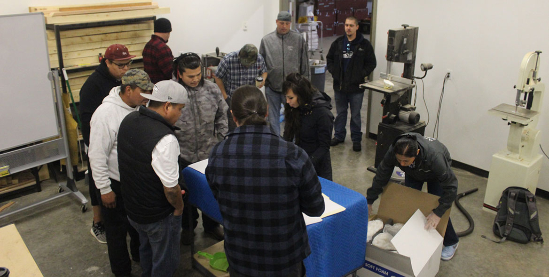A group of people crowd around a table to view Coast Salish tools and knives