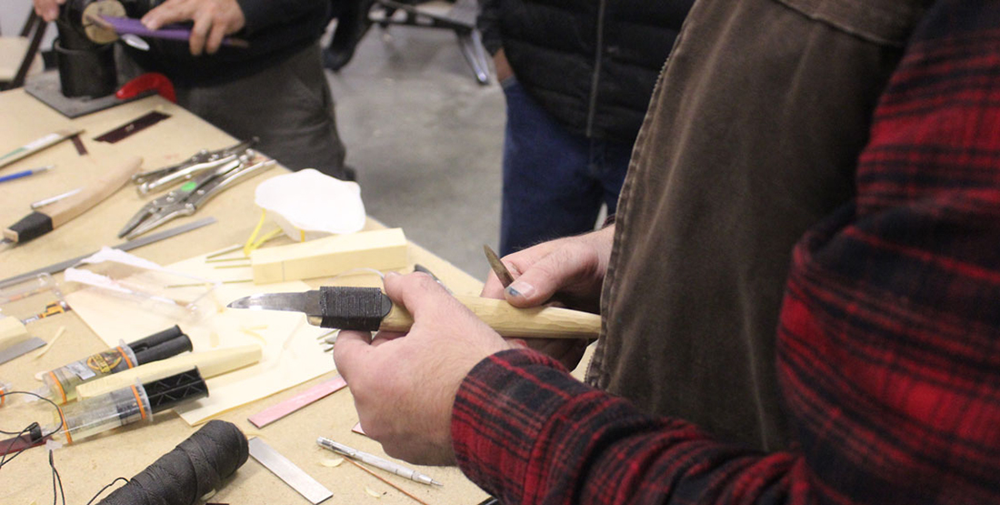 A hand holds a finished crooked knife with a wooden handle