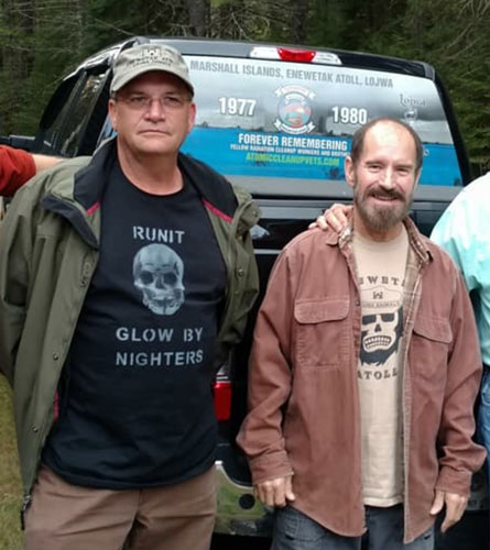 two men stand next to each other in front of the bed of a truck