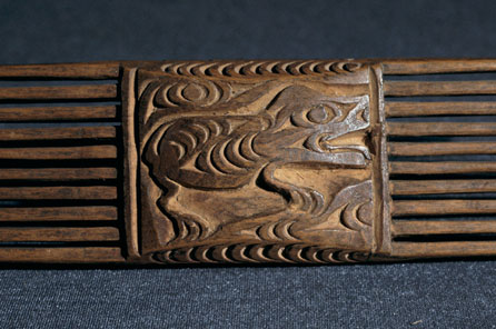 A coast salish art style comb decorated with a four-legged animal in clear profile, its tail curled up over the head and negative crescents and trigons defining the ribs