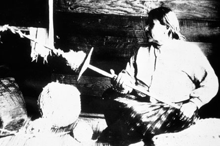 A 1915 photo showing a weaver named using a spindle with a whorl to spin wool