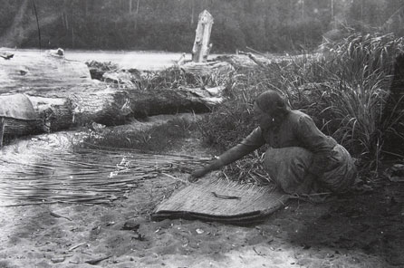A black and white photo of a woman weaving a cattail mat