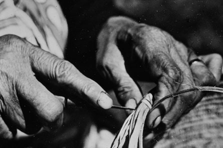 A black and white photo of a pair of hands using a hand tool to weave
