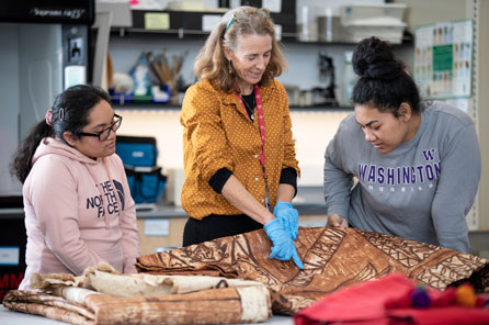 a teacher and students look at a cloth in the burke collections