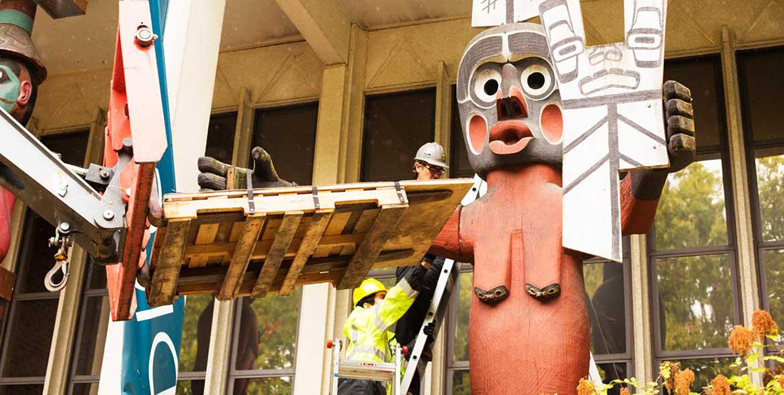 A forklift carefully approaches a large totem pole