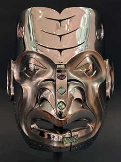 a carving of a face cast in bronze with abalone