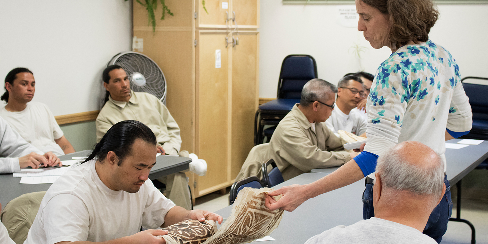 a woman points out details in a tapa cloth to a man sitting at a desk