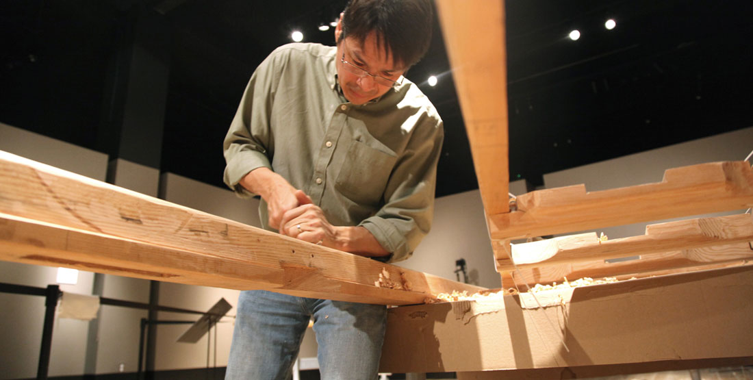 A researcher uses a hand tool to carve an Angyaaq boat