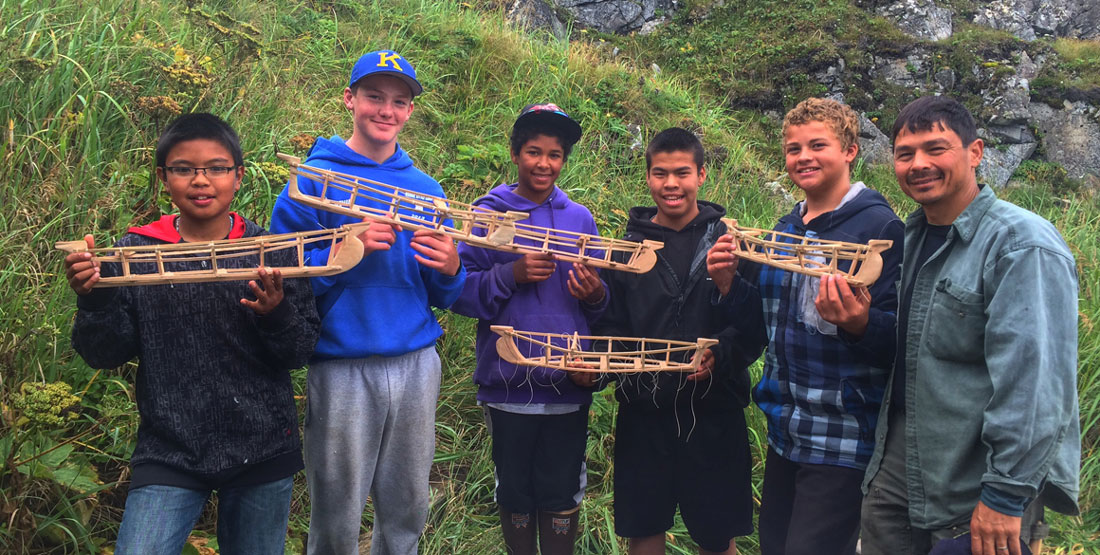 A researcher and five children stand outside holding model Angyaaq boats