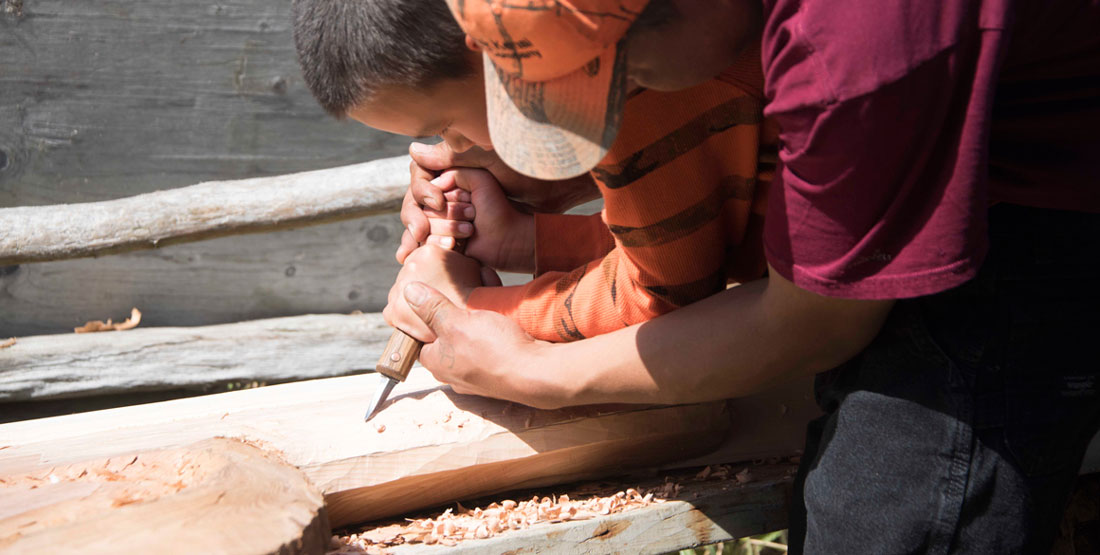 Two people use hand tools to carve wood