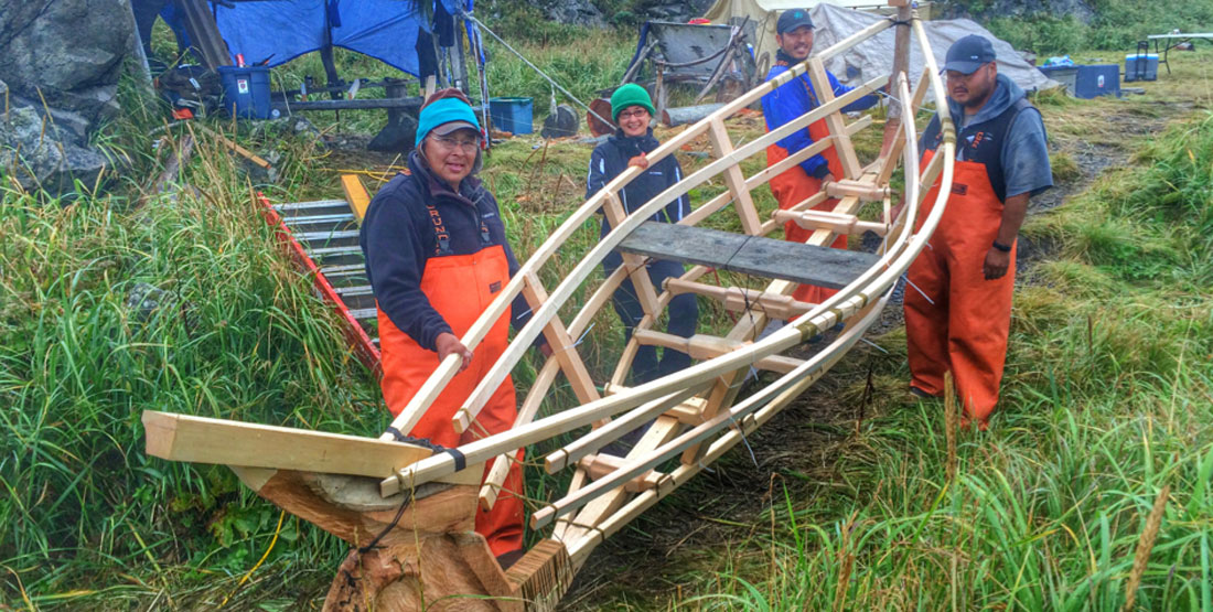 Four community members stand outside with the frame of the Angyaaq boat