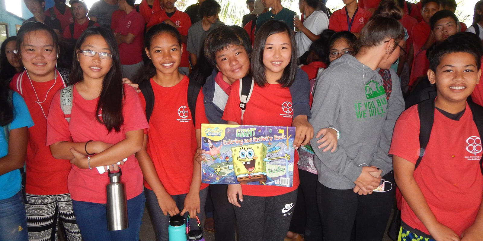 A group of schoolchildren wearing backpacks hold a picture of Spongebob Squarepants