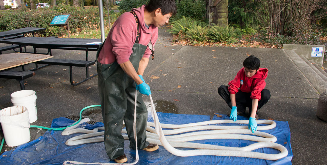 A researcher and a child stand on a blue tarp outside holding a long tubular-looking bear gut