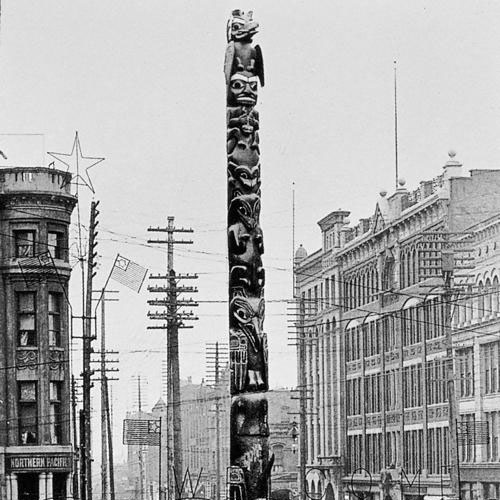 historic black and white photograph of a totem pole being erected in Seattle's Pioneer Square