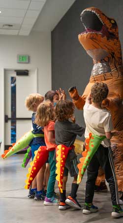 group of kids around a person in an inflatable t. rex costume