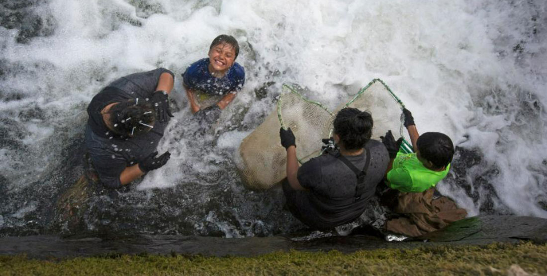 a young boy smiles while standing in a swift river with other youth