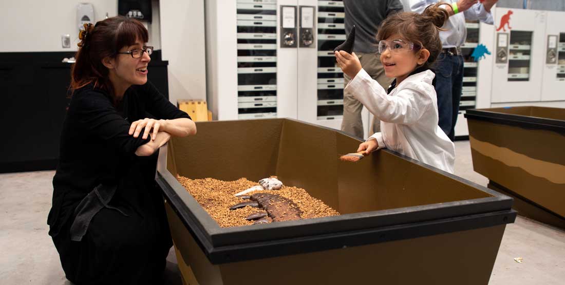 a burke educator and a kid interact at a dig pit with fossil casts