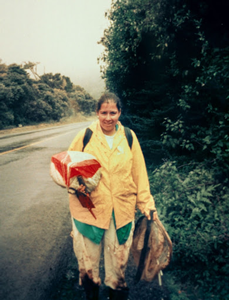 photo of gabriela chavarria working in the field, wearing a yellow rain coat and it appears to be raining