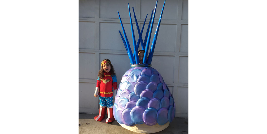 Two kids dressed up in costumes, one is Wonder Woman, the other an ancient spikey sea creature