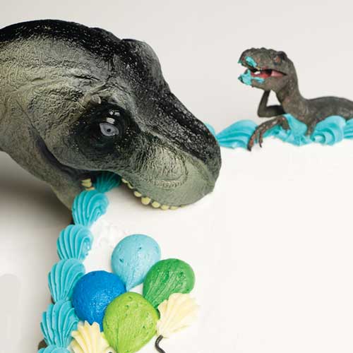 small toy dino figures eating cake with icing on their mouths