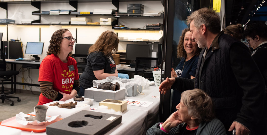 staff member talks to visitors through an open door with artifacts on a table in front of them