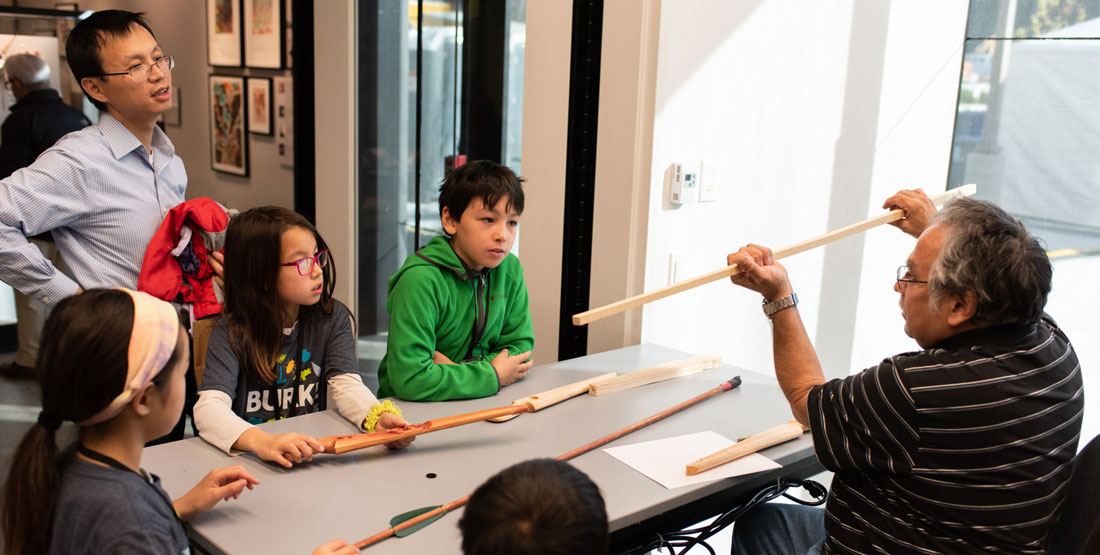 a man holds up a stick to show how an atlatl is carved