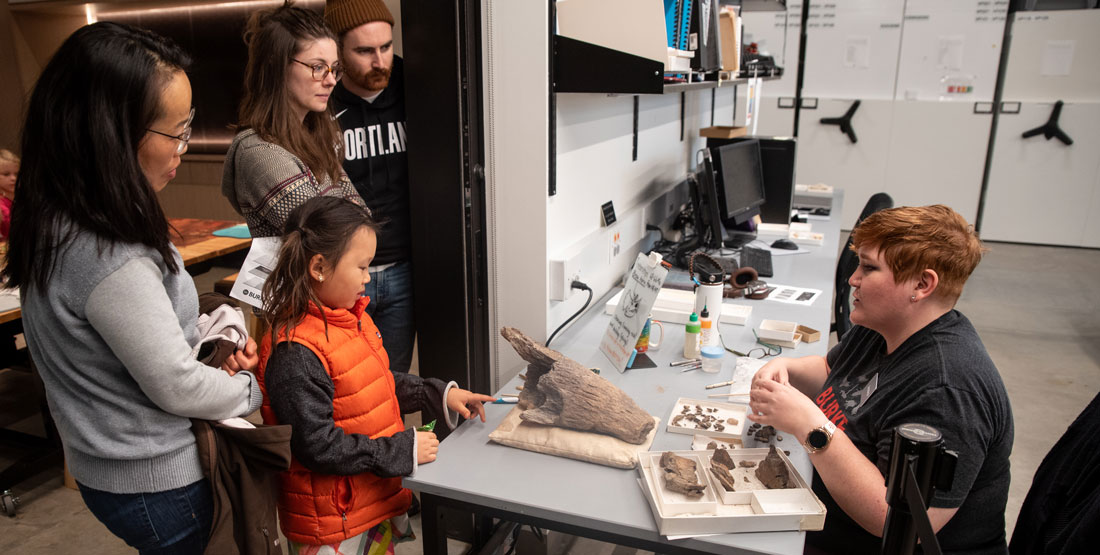 visitors stand near the open door and talk to a volunteer with fossils out on the table