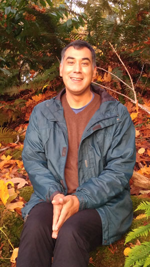 a man poses for a portrait with trees behind him