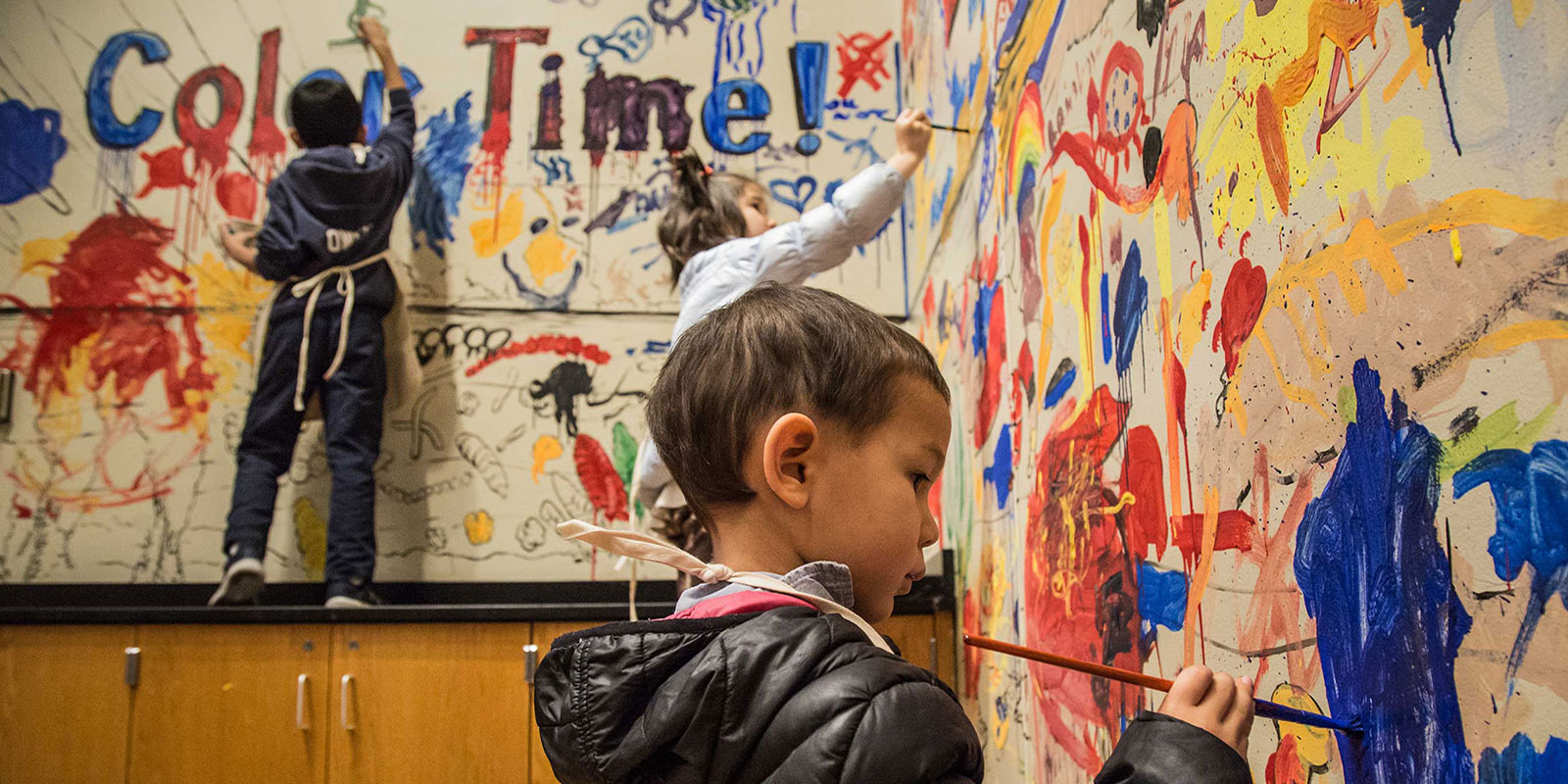 A preschool-age boy carefully paints blue paint on the walls of the Burke Museum