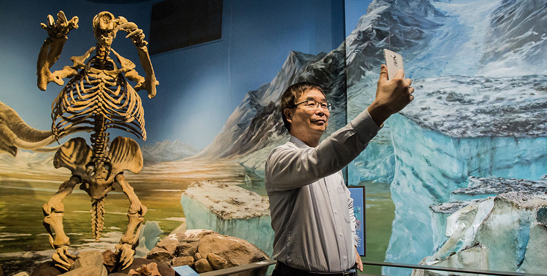 A man takes a selfie in front of a giant ground sloth