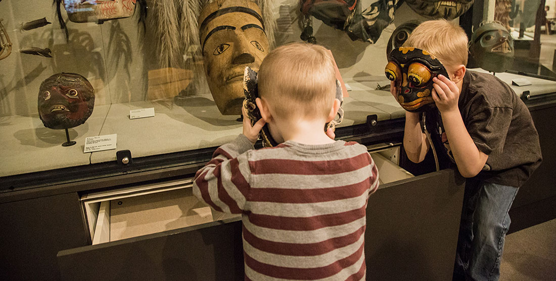 Two young boys hold masks up to their faces