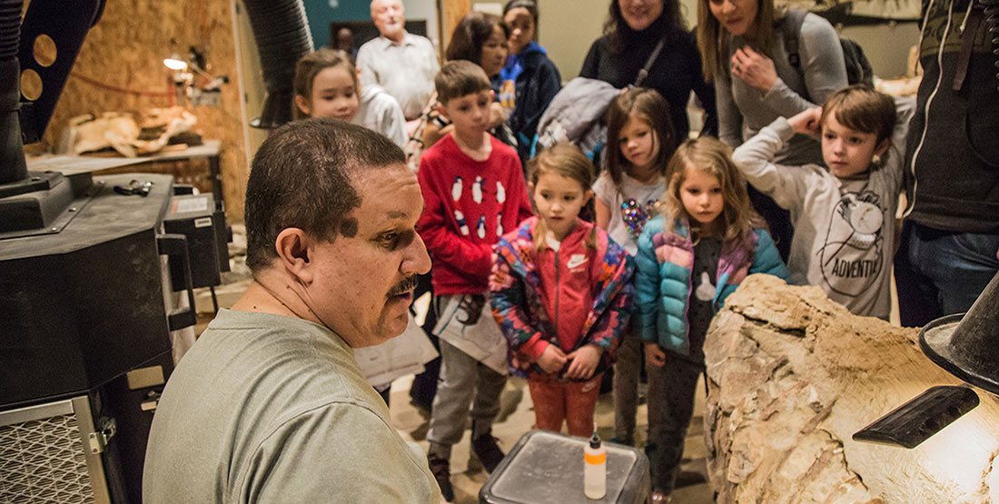 A man shows a large group of young children the fossil he's preparing