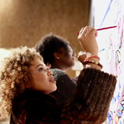 two women paint on a giant canvas on a wall