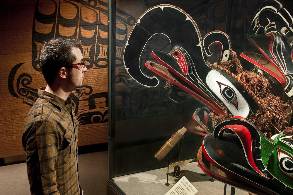 a man looks closely at native masks