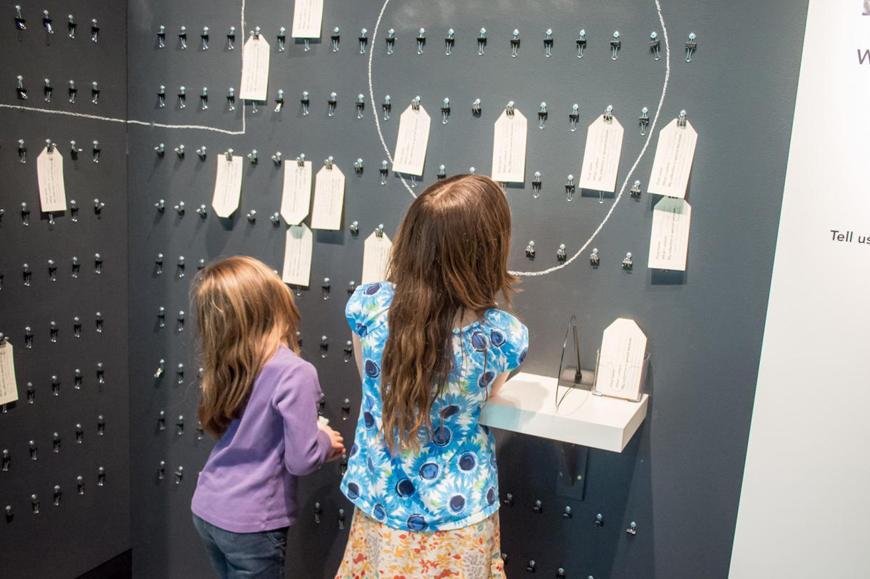 two girls look at collection tags hanging from a wall