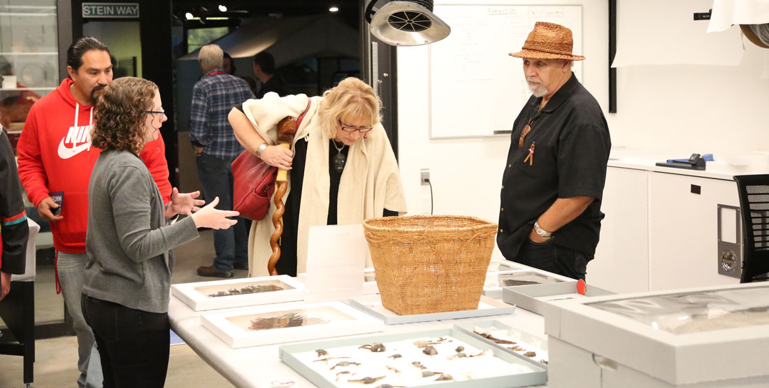 a burke researcher talks to visitors with a large basket and artifacts out on the table