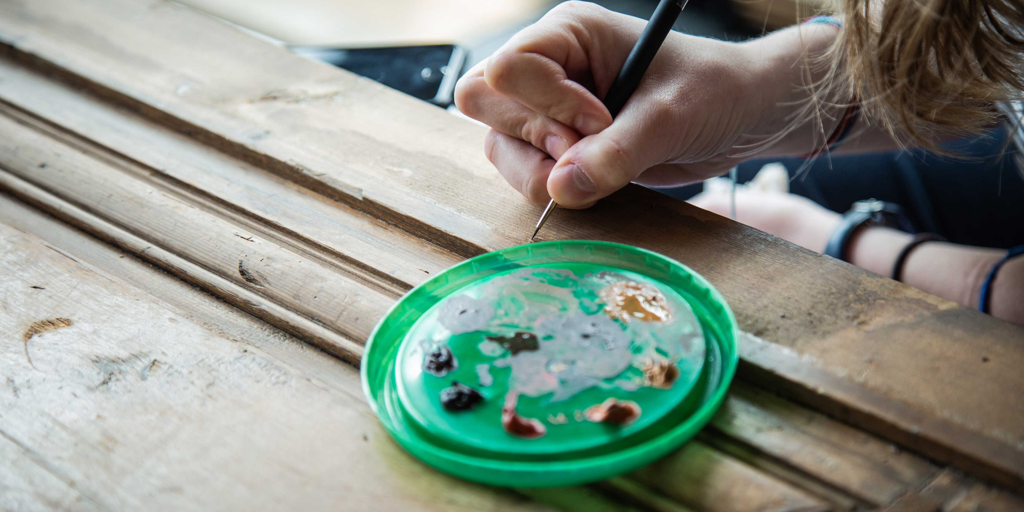 Close up of a woman's hand using a paintbrush to paint the wood