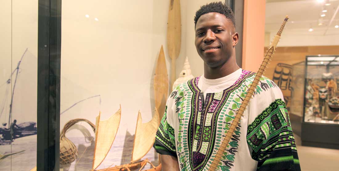 A young man holds a spear adorned with shark teeth from the Burke collection