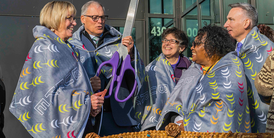 A group of people with giant scissors cut a cedar ribbon