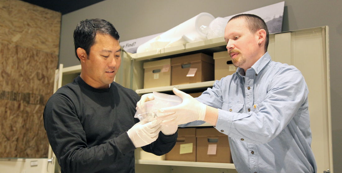 Two men wear gloves while removing an archaeological artifact from its bag