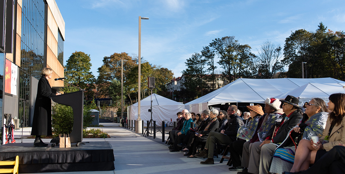 A woman talks at a podium to a crowd of people outside a museum