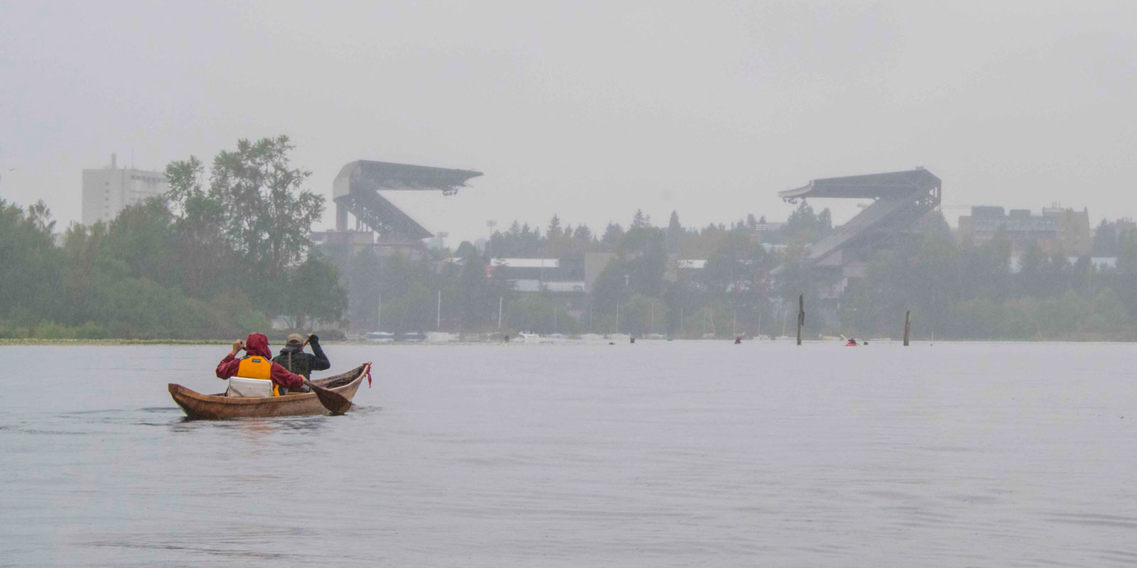 two men paddle a canoe with husky stadium in the background