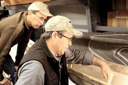 Two men look closely at the canoe details