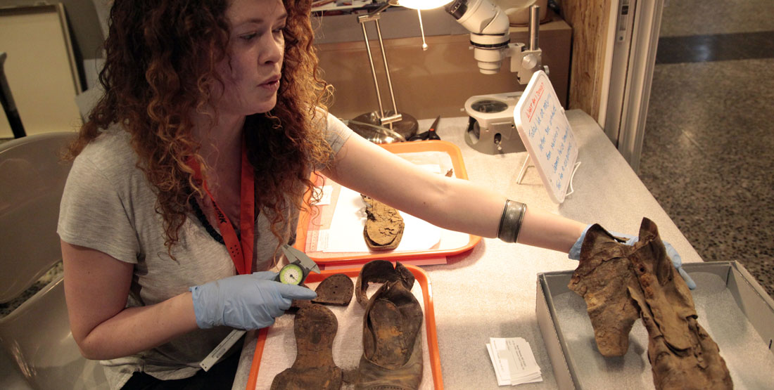 a young woman measures boot artifacts from an archaeological site