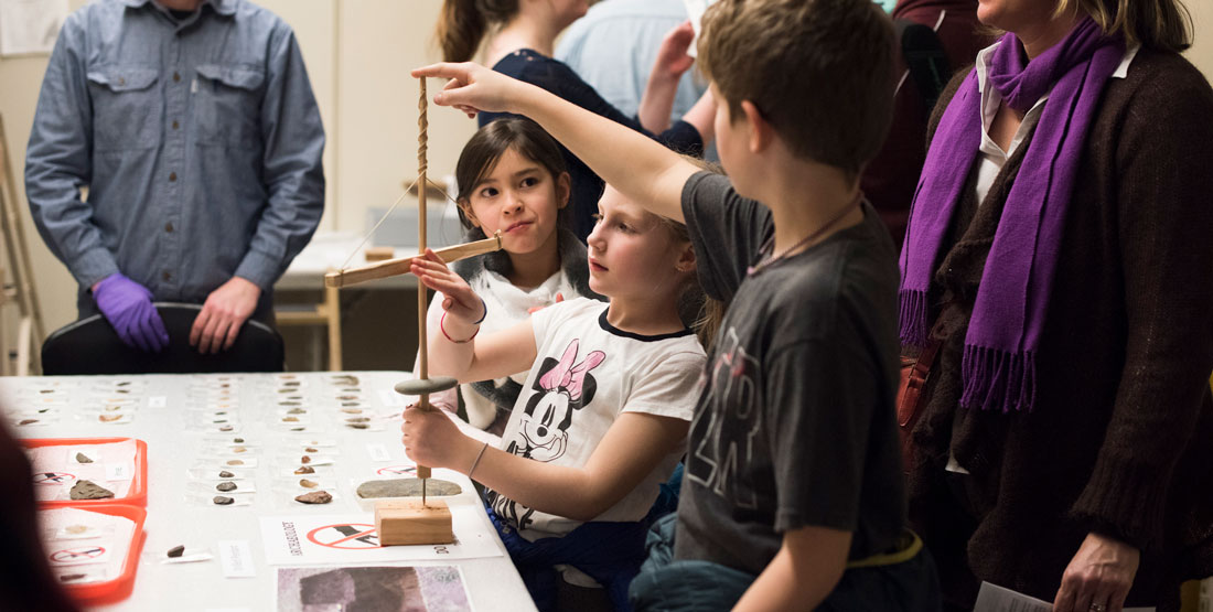 three young children hold a replica of a traditional tool to examine it closely